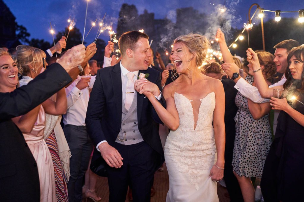 Bride an groom laughing heartily with each other as they finish walking through their sparkler run