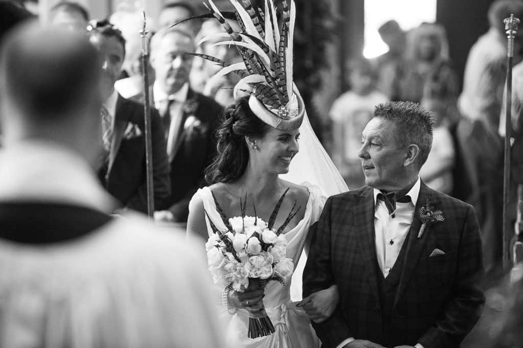 Father of the bride walking arm in arm with his daughter down the aisle as she wears a Vivienne Westward dress inspired by Gone With The Wind and complimentary headpiece featuring various long feathers