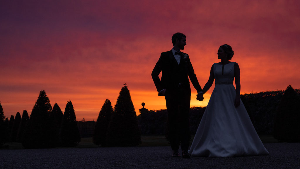 Bright red and orange sunset at Knowsley Hall with bride and groom silhouetted in foreground