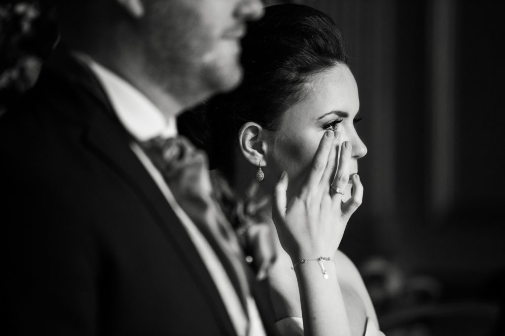 Bride wiping away emotional tear during wedding ceremony