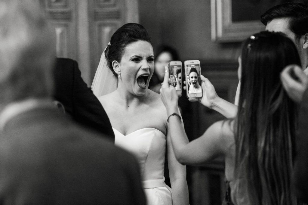 Bride open mouthed as guest takes pictures on two mobile phones