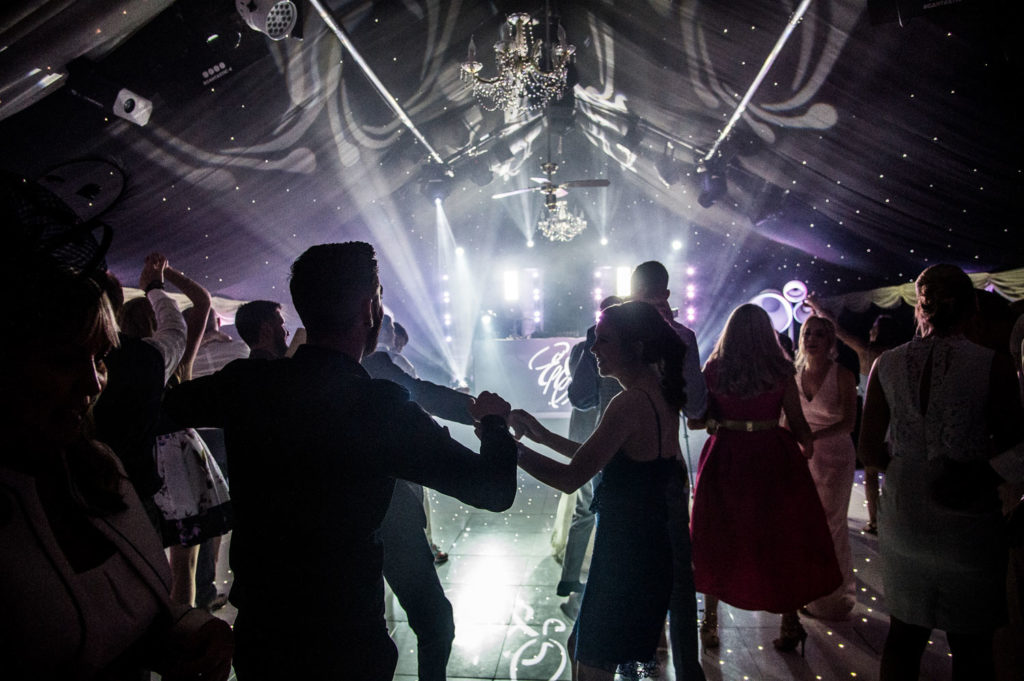 Guests dancing in silhouette as uplighters create dramatic backdrop in purple and white