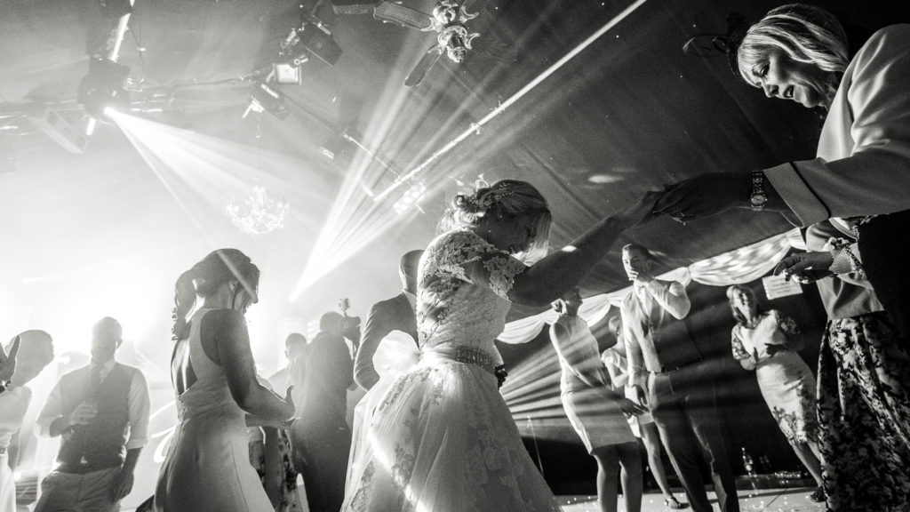 Black and white image of bride dancing with guests as laser lights streak through the scene