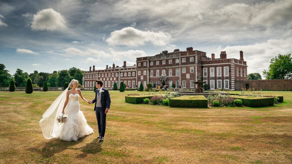 Bride and groom walking across the rear lawns at Knowsley Hall in the summer