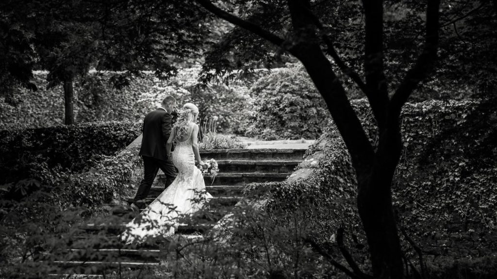 Bride and groom alone walking up garden steps away from camera