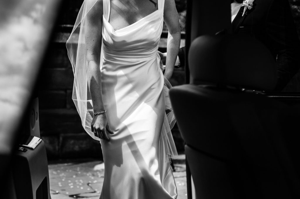 Bride's cowl neck silk dress captured through open back doors of wedding car as she approaches