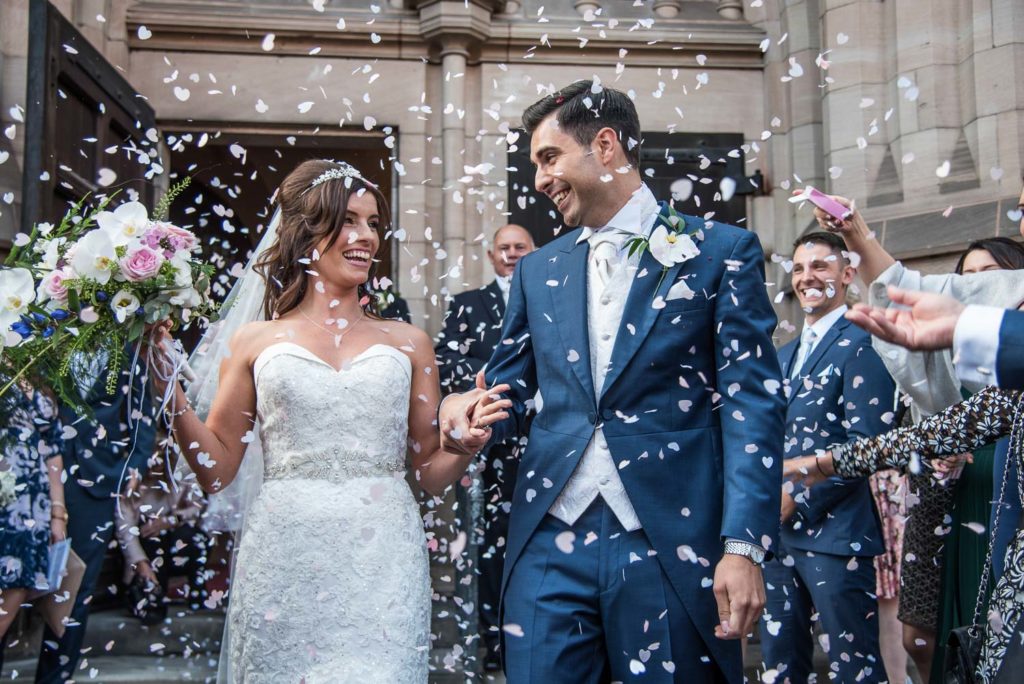 Bride and groom smiling at each other as they walk from ceremony into a confetti line