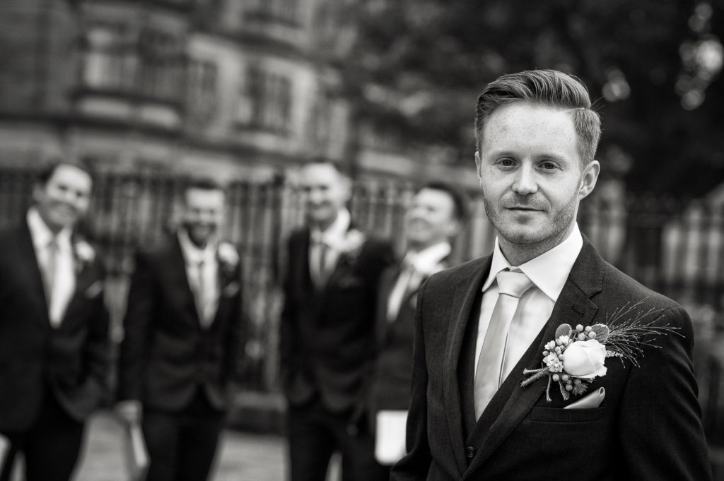 Groom portrait with groomsmen blurred in the background laughing