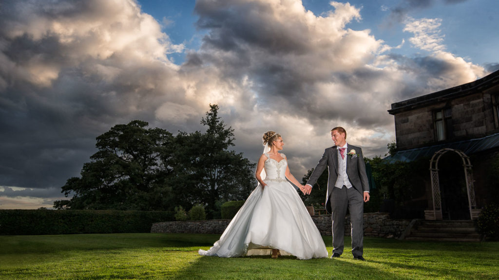 Bride and groom walking hand in hand across the lawn in the early evening with dramatic sky overhead