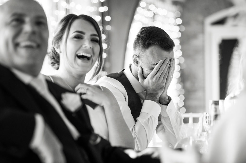Wedding breakfast speeches with bride laughing heartily and groom with his face in his hands