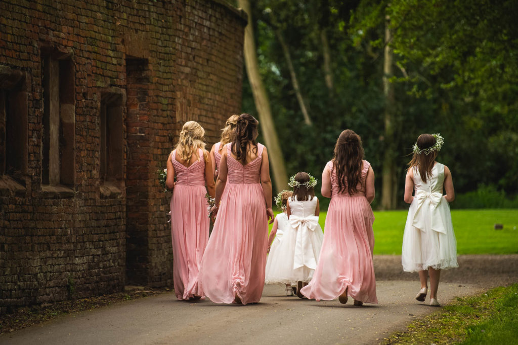 Bridesmaids in pink and flower girls in white walking away from camera heading to ceremony