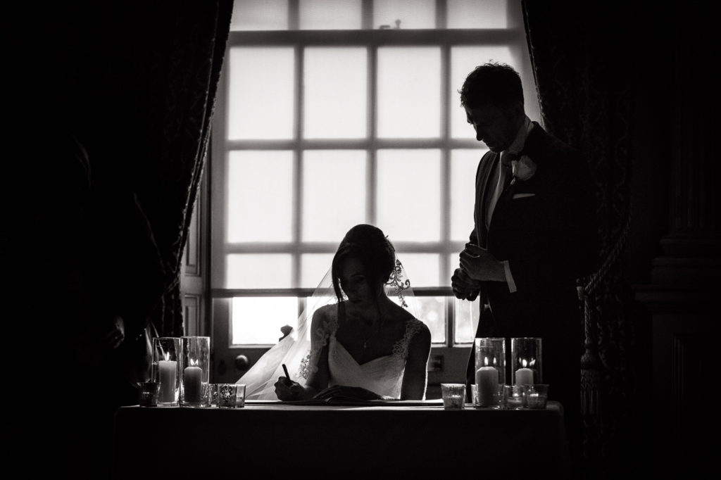 Monochrome Silhouette of Bride and Groom signing the register having exchanged vows at Knowsley Hall