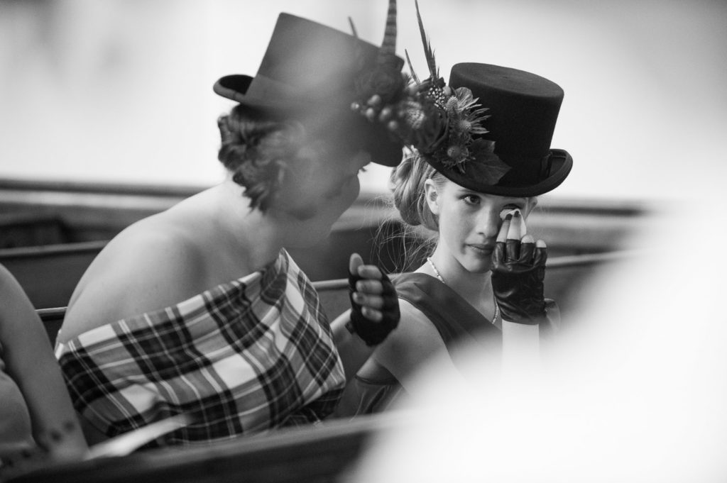 Bridesmaids wearing top hats adorned with feathers and berries wiping joyful tears away