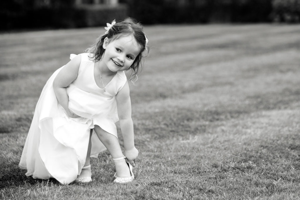 Young Flower girl on the lawn smiling cheekily adjusting her shoe from running around