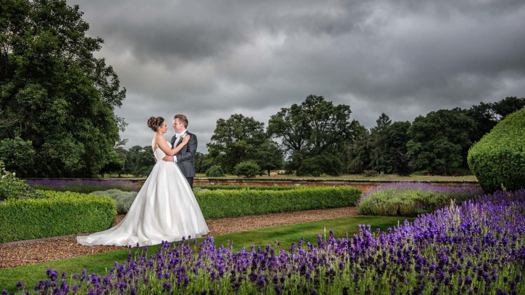 Bride and Groom featured in gardens at Iscoyd Park with moody grey sky and vibrant lavenders in bloom