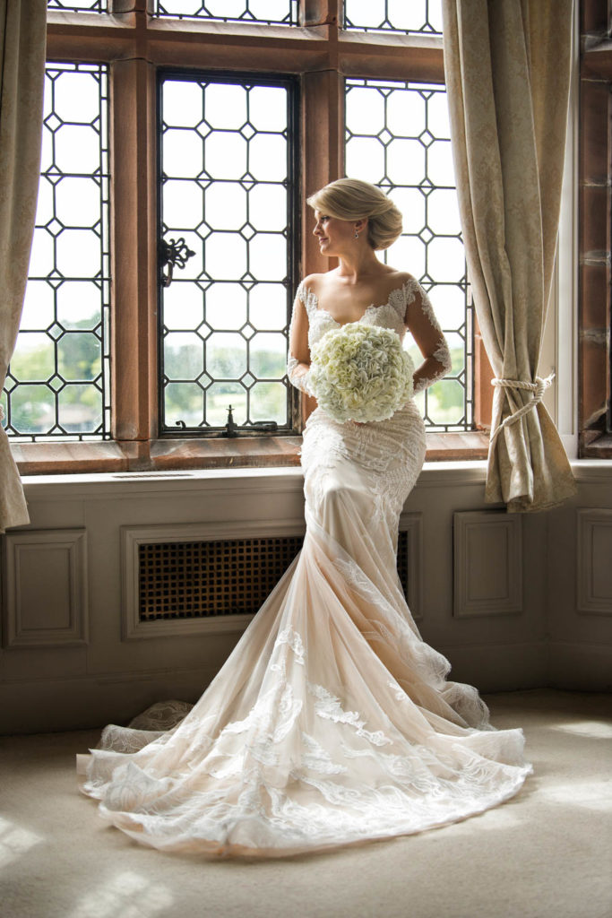 Bride sat on window seat with large bouquet taking a moment prior to her wedding