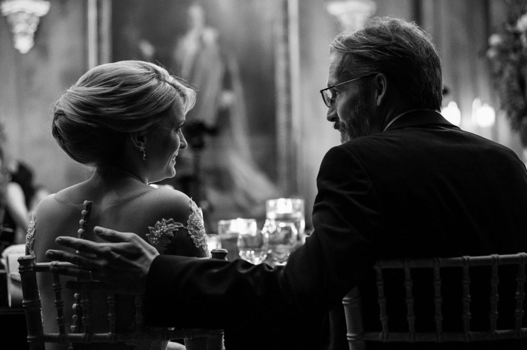 Bride and Groom at top table captured from behind as groom places his hand gently on her back