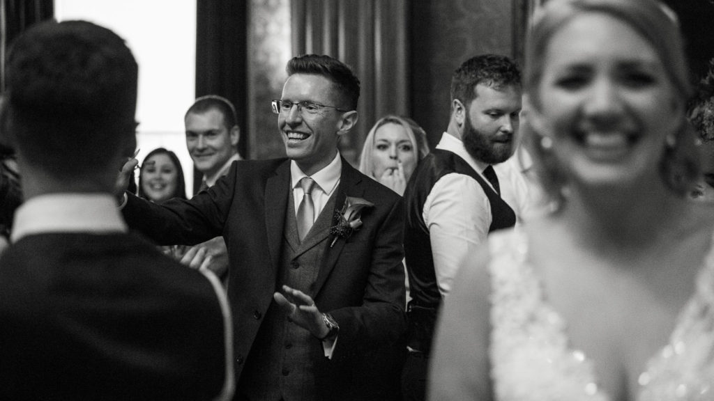 Groom beaming as he and his new wife enter the wedding breakfast with guests cheering their entrance