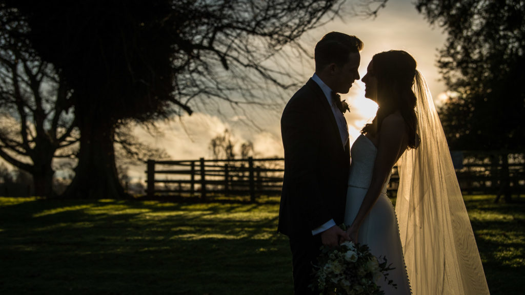 Bride and groom stand face to face in silhouette image during a soft sunset