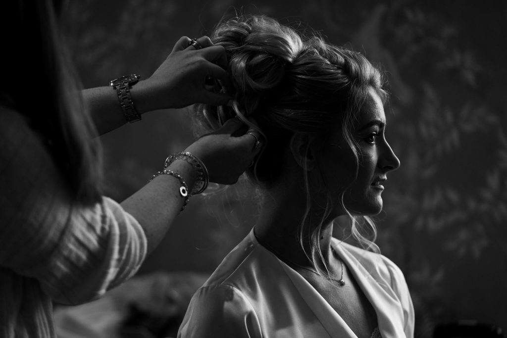 Profile close up in black and white of bride having finishing touches done to her undo