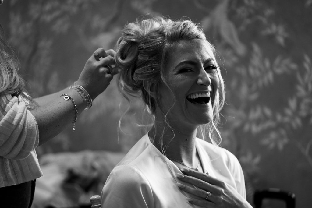 Bride laughing into camera as her hair is being finished