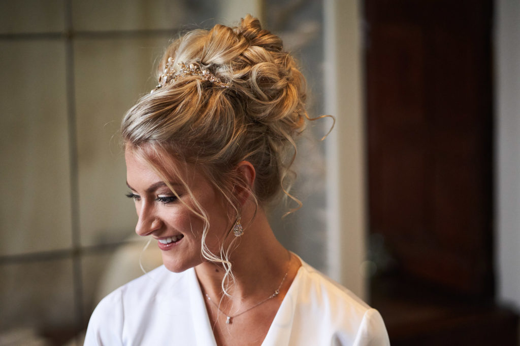 Detailed image of Bride's hair do with tussled curls in a large bun with gold, pearl and crystal hair strand