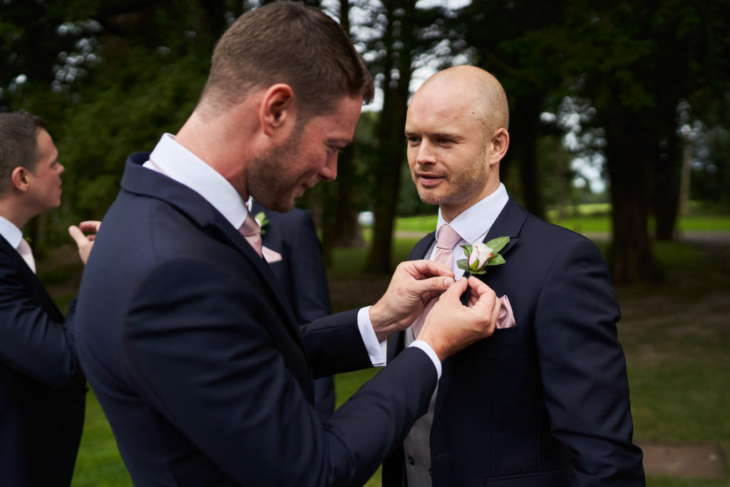 Ushers attaching their buttonholes of pale pink roses on each other prior to the ceremony