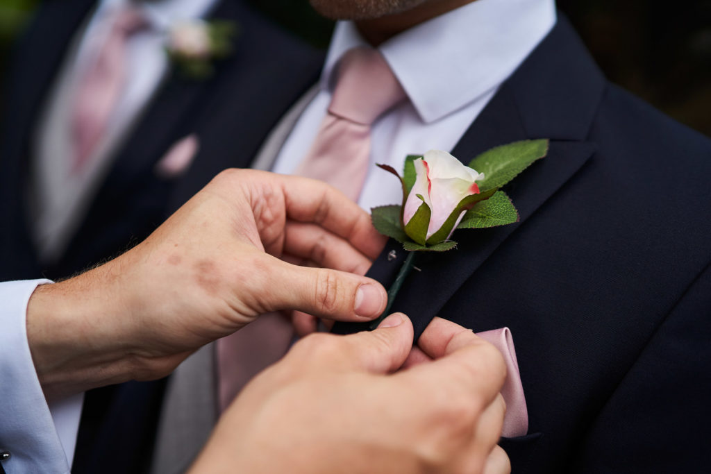 Close up of a pale pink rose buttonhole on a navy blue Morning Suit