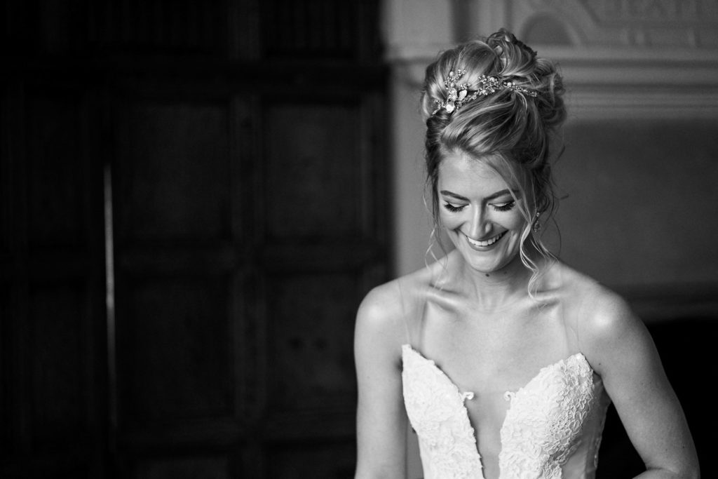 Bride looking down and laughing as her dress is being neatened