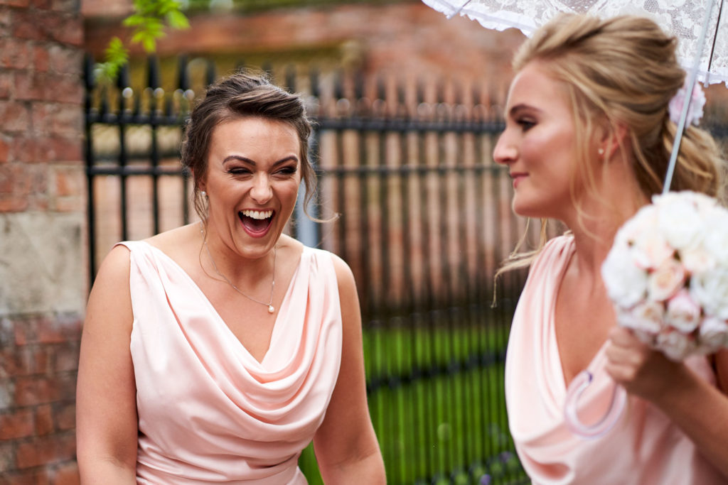 Bridesmaids stood under an umbrella laughing heartily while waiting