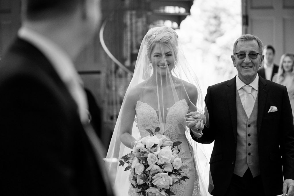 Father of the bride holding his daughter's hand as she smiles to her Fiancé as she approaches