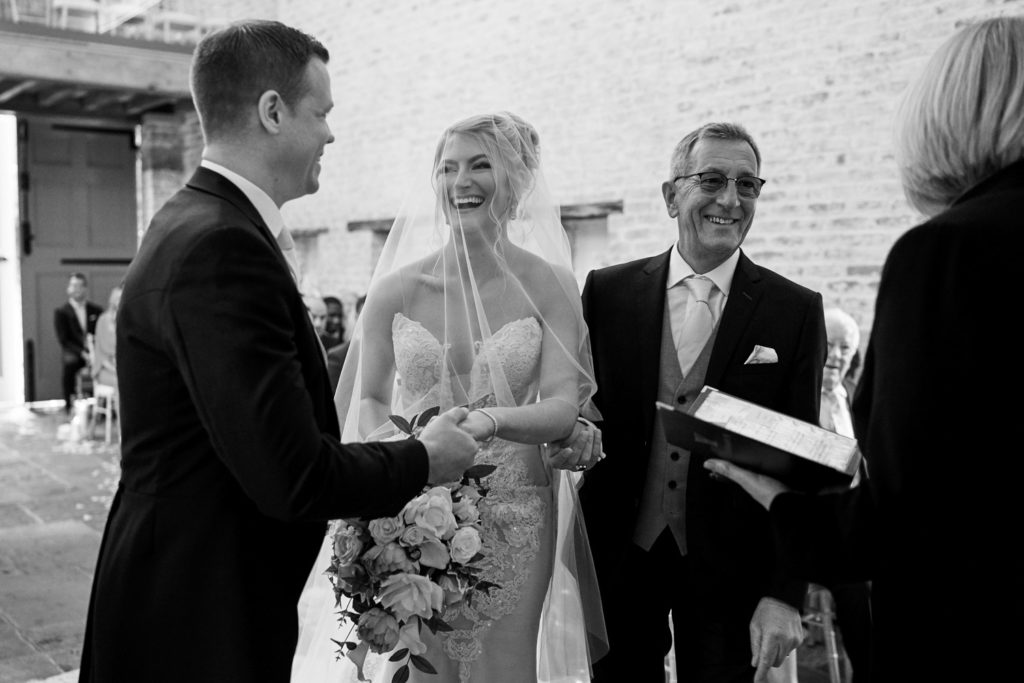 Father of the bride laughing with registrar as he gives his daughter's hand to her husband to be
