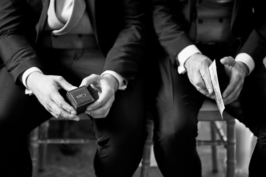 Hands of best man holding the ring box while groom holds his order of service