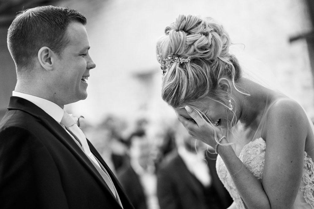 Bride and groom laughing as bride holds her hand to her face trying to compose herself