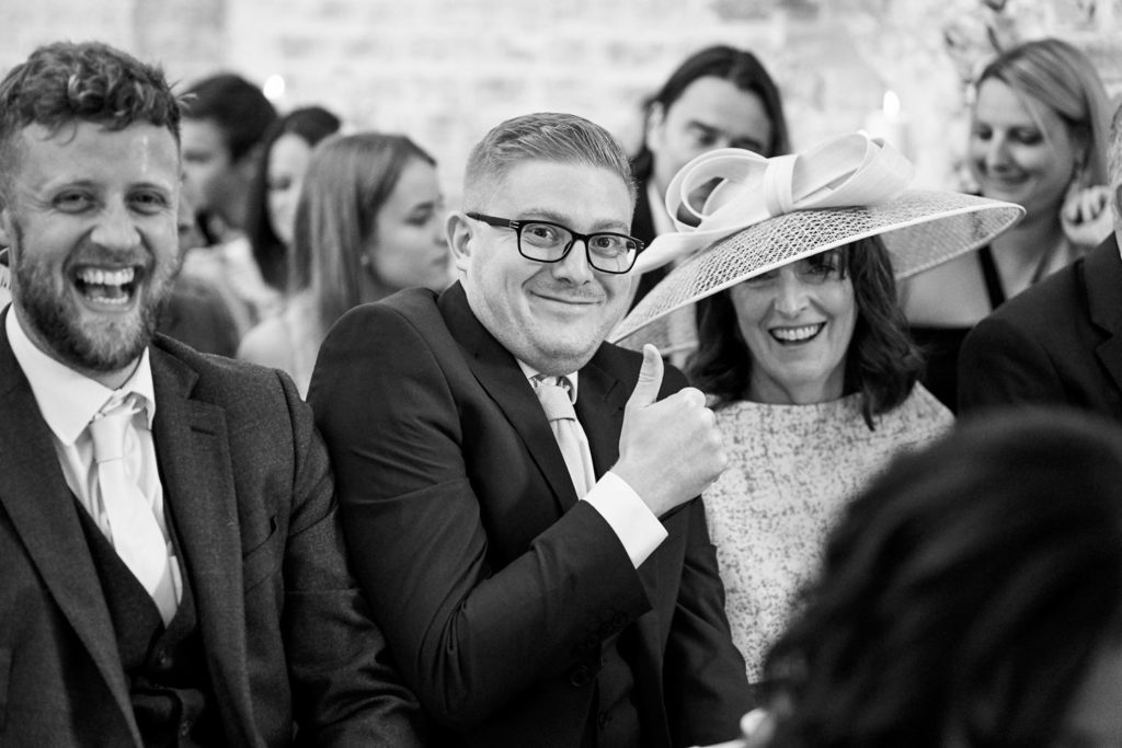 Guests laughing and giving a thumbs up as they wait for Bride and groom to sign the register
