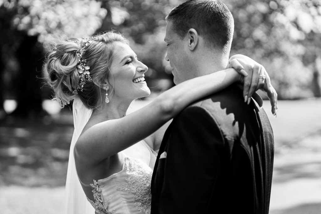 Bride posed with arms wrapped loosely around groom's neck as they gaze lovingly at each other