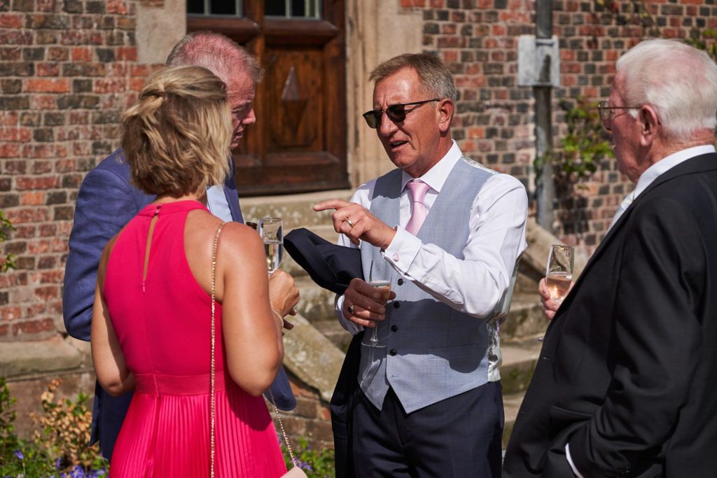 Father of the bride chatting with guests with his jacket under his arm and sunglasses on