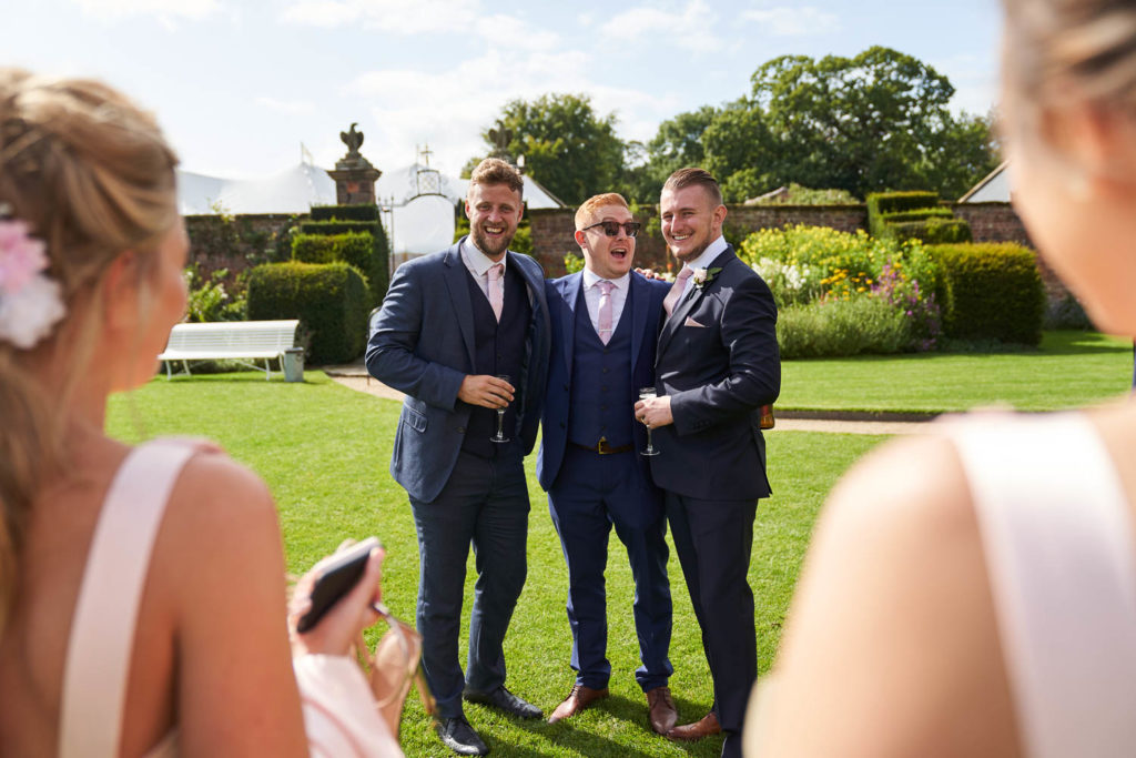 Groomsmen posing for mobile phone pictures by bridesmaids