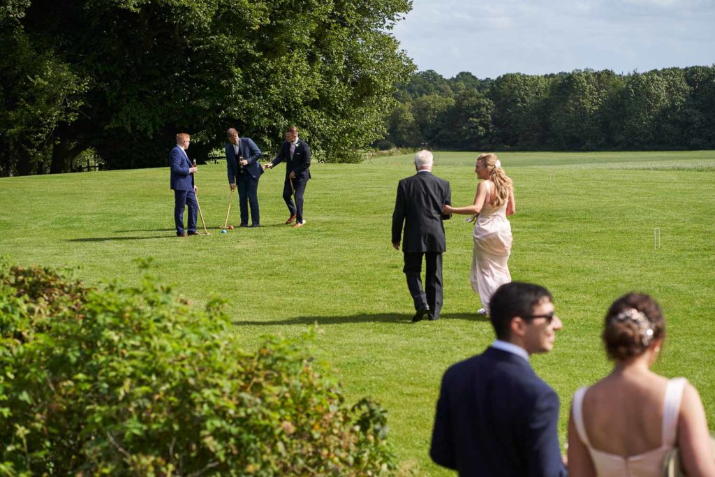 Groomsmen making an effort to play croquet on the lawn