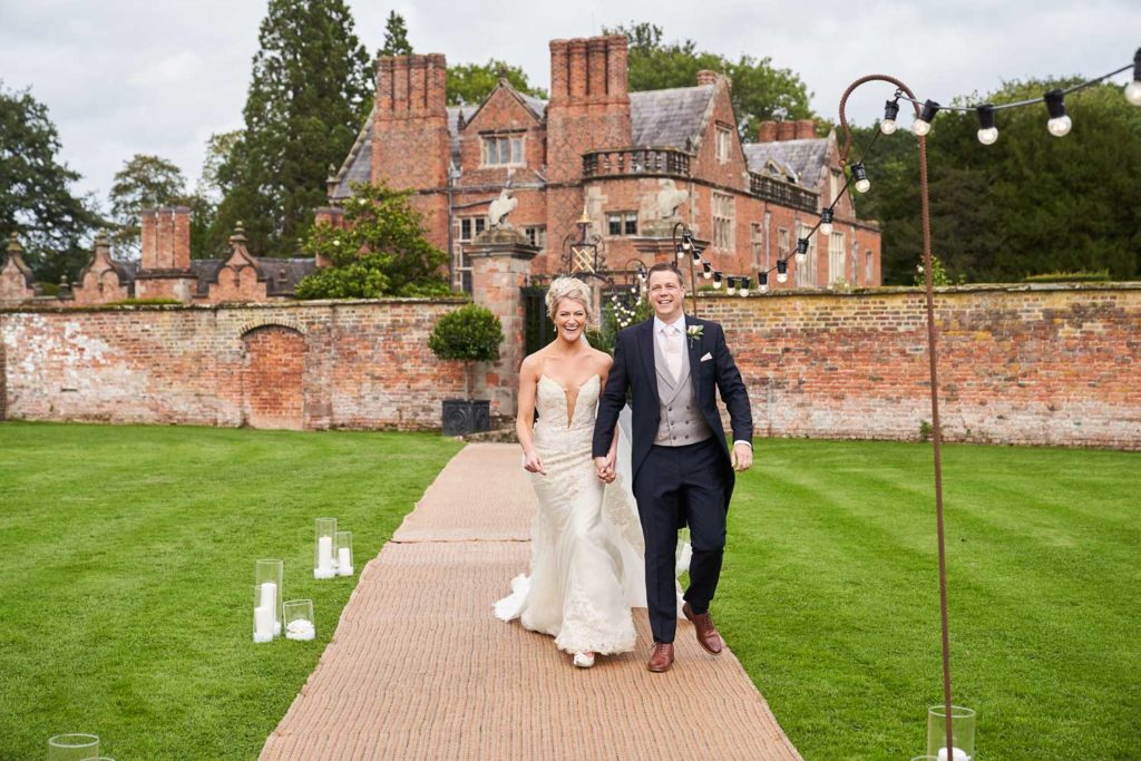 Bride and groom walking along a garden path lined with fairy lights and candles