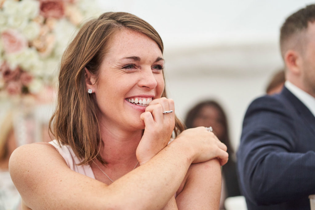 Bridesmaid laughing with her hand up to her mouth during speeches