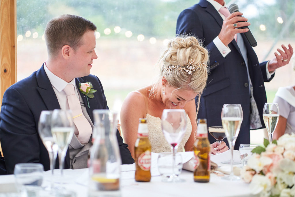 Bride giggling with embarrassment as her father gives his speech