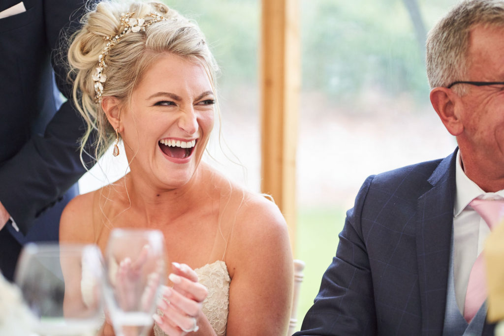 Bride laughing at a guest on the top table during Groom's speech
