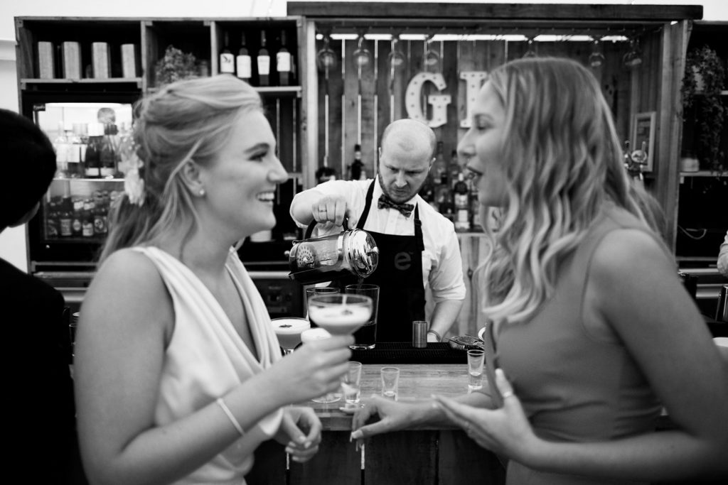 Guests at the bar providing a blurry foreground as the bar tender becomes the focus making cocktails