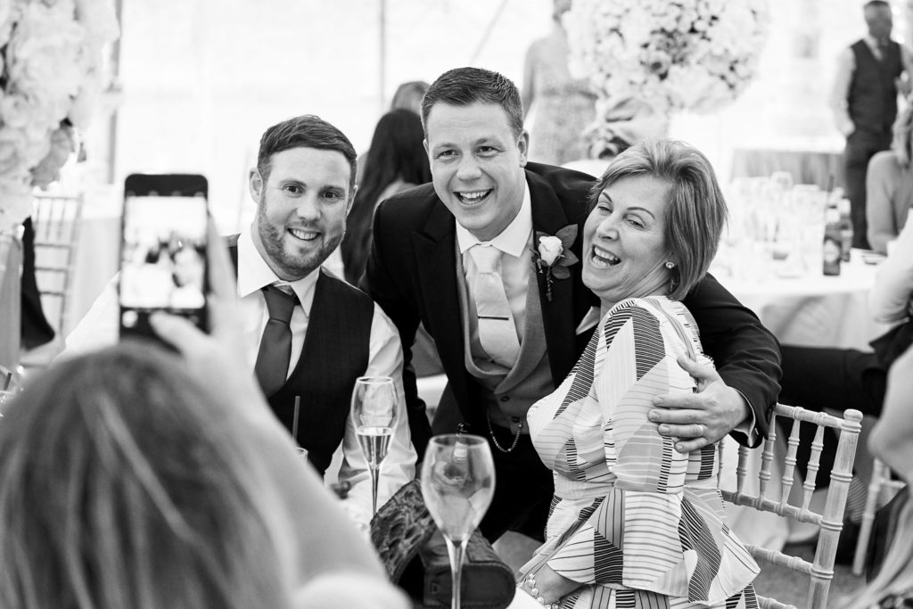 Groom posing for a mobile phone picture with guests