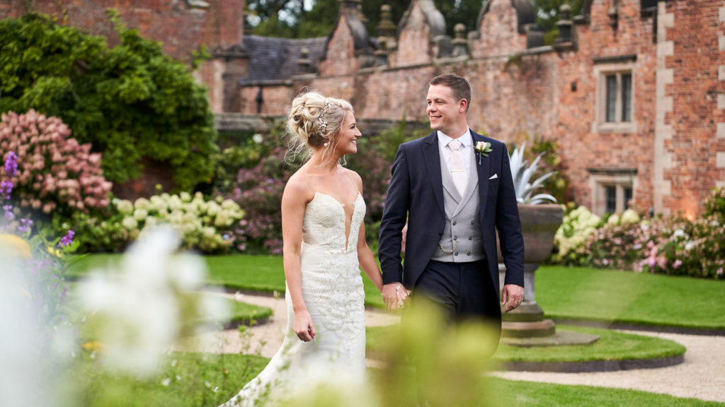 Happy couple walking hand in hand through the gardens at Dorfold Hall