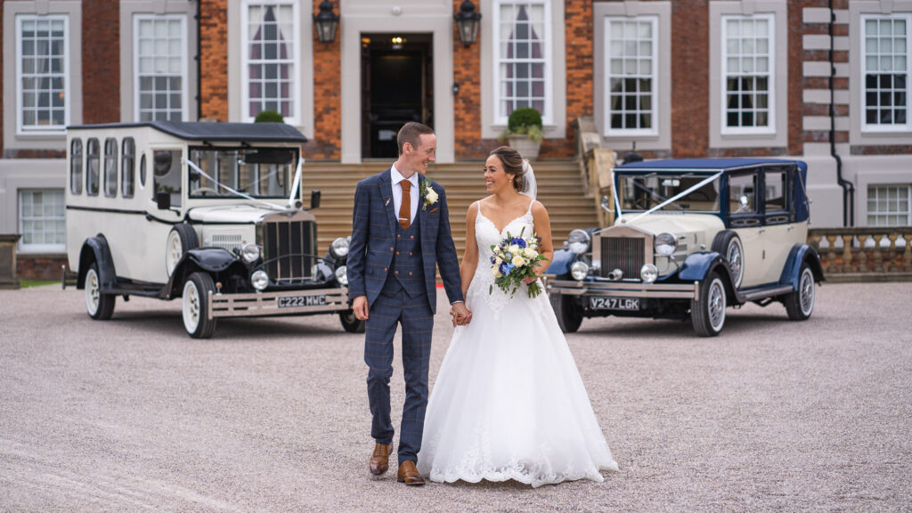 Brdie & Groom walking with Knowsley Hall as their backdrop and the Wedding Cars.