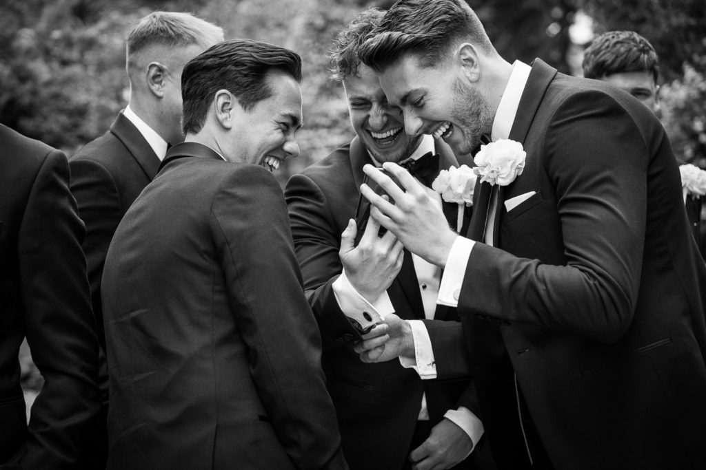 Ushers huddled together looking at a mobile phone laughing together before the church wedding ceremony