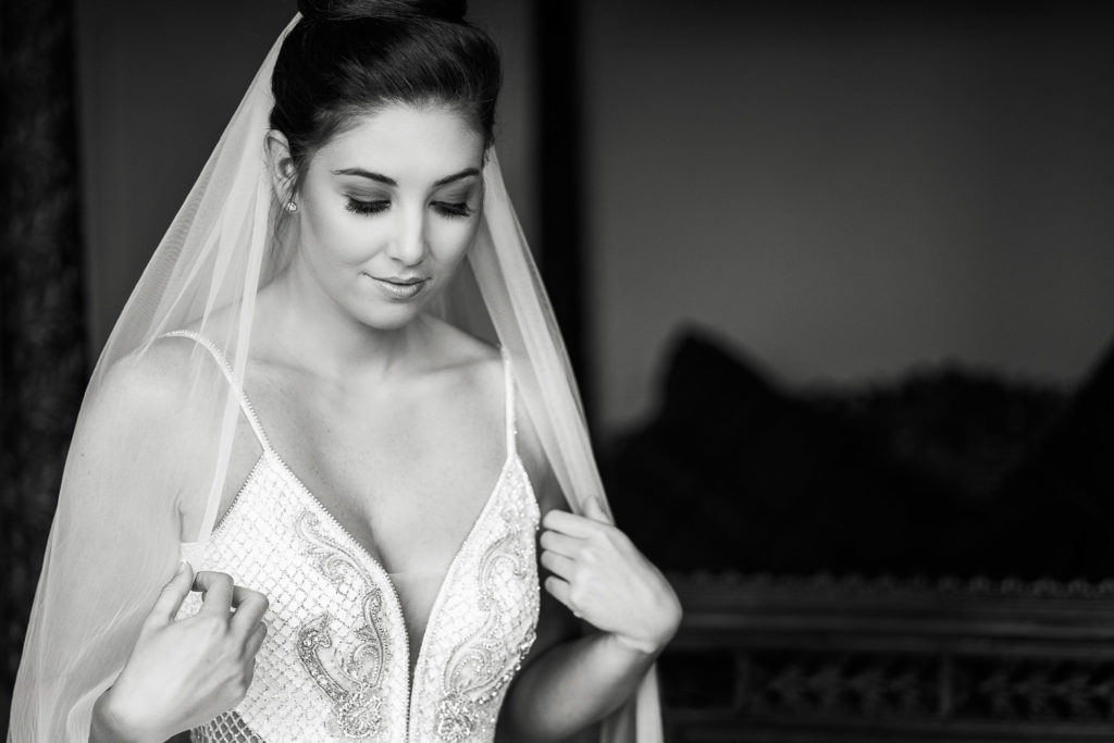 Black and white image of a beautiful bride glancing down as she fixes her veil during last moments of bridal preparation