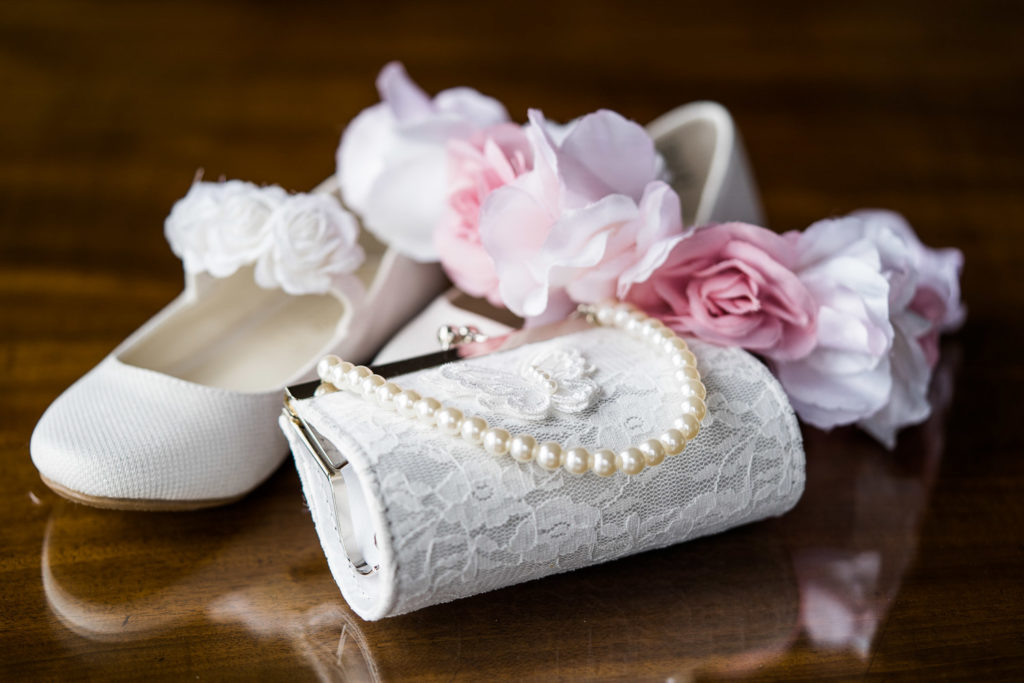 Flower girl accessories of white shoes and lace clutch bag with pink floral headdress and string of pearls